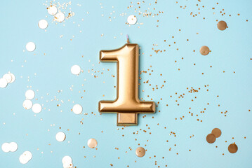 Gold candle in the form of number one on blue background with confetti.