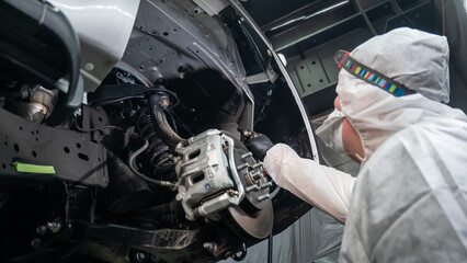 An auto mechanic applies anti-corrosion mastic to the underbody of a car. - obrazy, fototapety, plakaty