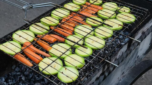 Chopped zucchini and carrots roasting on fire seasoned with aroma herbs and spices. Delicious fresh vegetables grilling on barbecue smoker grid. Diet vegan bbq. Outdoor recreation in backyard 