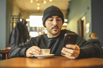 A man in a cafe drinks coffee and reads the news on the phone. Scrolling. Rest in a cafe. Leisure.