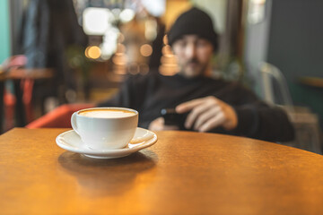 A man in a cafe drinks coffee and reads the news on the phone. Scrolling. Rest in a cafe. Leisure.