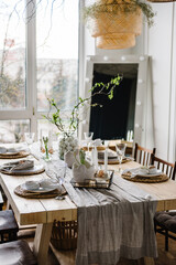 Interior design of easter dining room. Happy easter dinner with decor at home. Minimalist composition in living room with copy space, hanging lamp, candles, easter eggs, vase with twig, branch, leaves