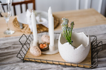 Easter decor with candles, easter quail eggs in nest, vase with flowers at home. Setting table for...