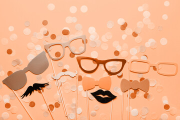 Photo booth props glasses, mustache, lips on a pink background flat lay. New trending PANTONE Peach Fuzz colour of 2024 year