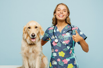 Young happy veterinarian woman she wear uniform stethoscope heal exam hug embrace retriever dog point finger up isolated on plain pastel light blue background studio portrait. Pet health care concept.