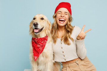 Young owner woman wear casual clothes red hat bandana hug cuddle embrace her best friend retriever dog show v-sign gesture isolated on plain pastel blue background studio. Take care about pet concept.
