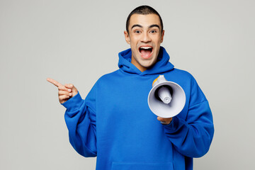 Young surprised middle eastern man wears blue hoody casual clothes old in hand megaphone scream announces discounts sale Hurry up point finger aside on area isolated on plain solid white background. - obrazy, fototapety, plakaty