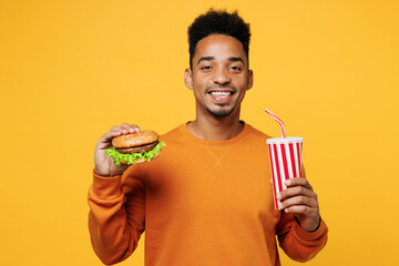 Young fun happy man wear orange sweatshirt casual clothes hold eat burger drink cola soda pop hold...