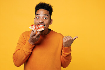 Young man wear orange sweatshirt casual clothes hold eat slice of slim italian pizza point finger aside isolated on plain yellow background Proper nutrition healthy fast food unhealthy choice concept - obrazy, fototapety, plakaty