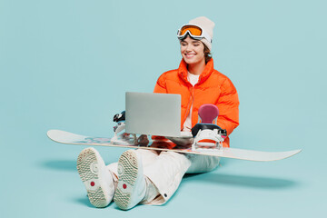Full body fun young IT woman wear windbreaker jacket hat ski goggles mask sit with snowboarding...