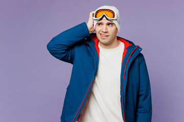 Skier confused man wear warm blue windbreaker jacket ski goggles mask hold scratch head look aside spend extreme weekend winter season in mountains isolated on plain purple background. Hobby concept.