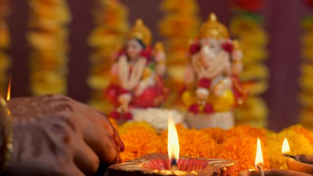 Indian woman hand placing diya in front of Hindu Gods - Diwali  idol worship  festival of lights  religious ritual. Family preparing for Deepawali puja - colorful flowers  Lord Ganesh  Devi Laxmi  ...