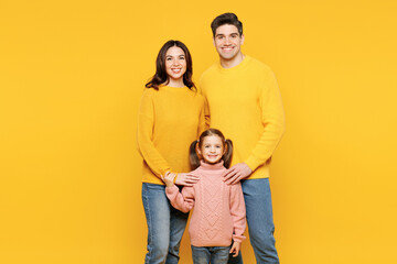 Full body young smiling cheerful happy parents mom dad with child kid girl 7-8 years old wear pink sweater casual clothes hug cuddle look camera isolated on plain yellow background Family day concept