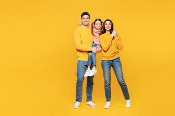 Full body young fun happy parents mom dad with child kid girl 7-8 years old wear pink sweater casual clothes hold little daughter look camera isolated on plain yellow background. Family day concept.