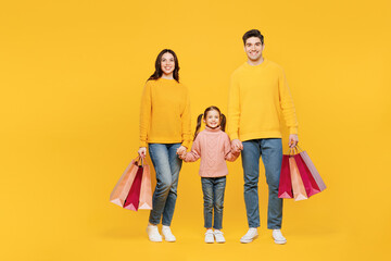 Full body young happy parent mom dad with child kid girl 7-8 year old wear pink sweater casual clothes hold shopping package bags isolated on plain yellow background Black Friday sale buy day concept