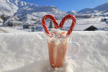 A steaming mug of hot cocoa on a snowy windowsill with winter mountains in the backdrop