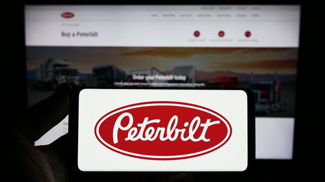 Stuttgart, Germany - 12-27-2023: Person holding smartphone with logo of US truck manufacturing busniess Peterbilt Motors Company in front of website. Focus on phone display.