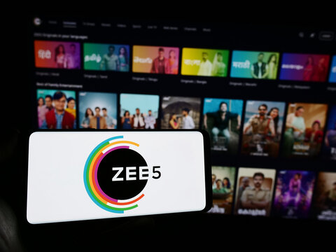 Stuttgart, Germany - 12-27-2023: Person holding mobile phone with logo of Indian video streaming platform company ZEE5 in front of business web page. Focus on phone display.