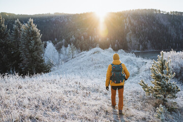 Trekking in winter mountains against the background of the glare of the sun, winter hiking, man walking down the road, tourist route in the mountains.