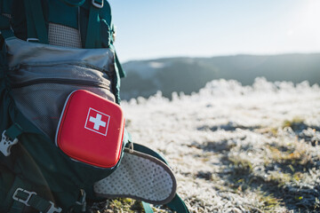 A red first aid kit is on the backpack, tourist equipment. - obrazy, fototapety, plakaty
