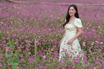 Obraz na płótnie Canvas beautiful woman in dress enjoying blooming pink globe amaranth or bachelor button field