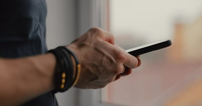 Close-up of male hands in bracelets is using a mobile phone, writes message on his smartphone