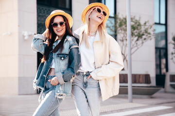 Two young beautiful smiling hipster female in trendy summer clothes. Carefree women posing in the street. Positive models having fun outdoors at sunny day. Cheerful and happy. In hat and sunglasses