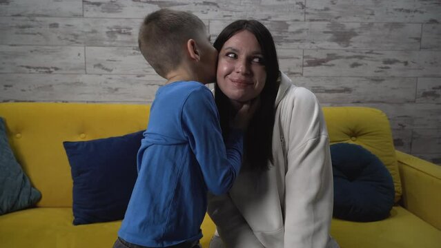 Medium shot. Son tells his mother secret, whispers in her ear, gossips about his personal life in the room, the mother smiles and hugs her son. spends free time together at home