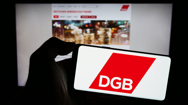 Stuttgart, Germany - 12-29-2023: Person holding cellphone with logo of German organization Deutscher Gewerkschaftsbund (DGB) in front of webpage. Focus on phone display.