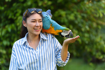 happy woman feeding blue-and-yellow macaw (Ara ararauna) bird on hand