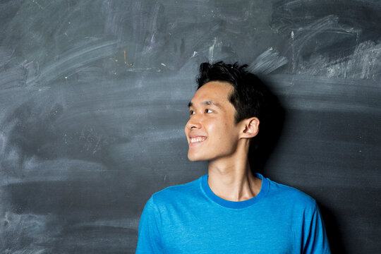 Happy Asian man looking to left next to a blackboard.