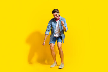 Full body photo of optimistic cool man dressed denim shirt shorts in glasses dancing on black friday isolated on yellow color background