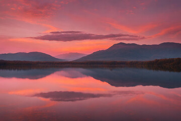 Fototapeta premium A sunset over a calm lake, with the sky painted in hues of orange and pink