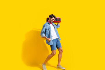Full body photo of good mood man dressed denim shirt shorts in glasses dance with boombox on shoulder isolated on yellow color background