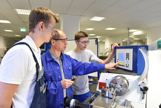 young apprentices in technical vocational training are taught by older trainers on a cnc lathes machine