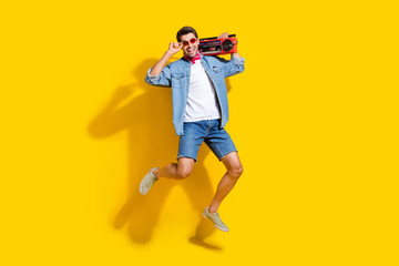 Fototapeta na wymiar Full body photo of cheerful man dressed denim shirt flying touch glasses hold boombox at summer event isolated on yellow color background