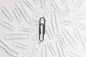 close up of one black paperclip and many white paperclips over white background