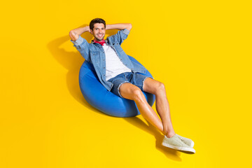 Photo of relaxed satisfied guy wear jeans jacket shorts lie on pouf hold arms behind head isolated...