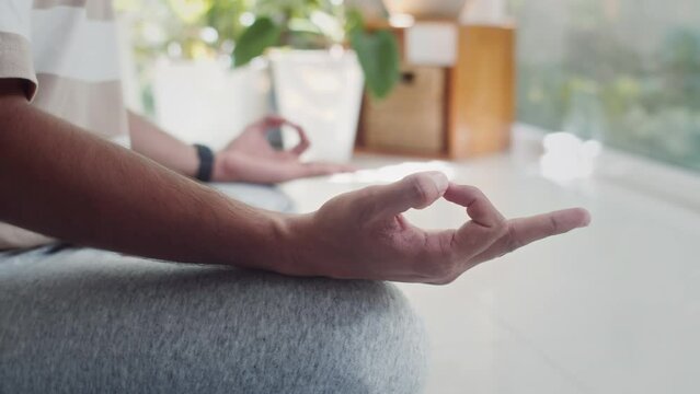 Handheld close up shot of hands of male yogi sitting in lotus pose while meditating in living room alone