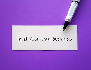 On purple background, pen writing on paper MIND YOUR OWN BUSINESS, to tell someone rude way to stop...