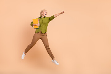 Fototapeta na wymiar Full size photo of nice girl wear khaki shirt flying hold copybooks clenching fist look empty space isolated on pastel color background