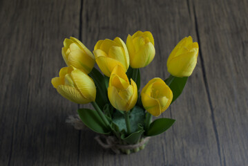 Obraz premium Artificial yellow tulips flowers on wooden table.