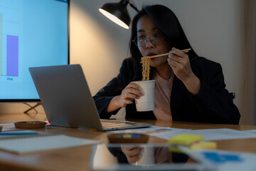 A businesswoman working late into the night and eating instant noodles