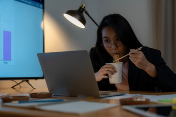 A businesswoman working late into the night and eating instant noodles © virojt