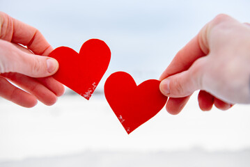 Hands holding red hearts on winter background.