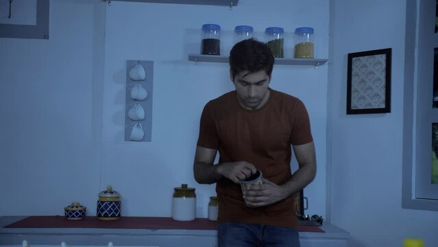 Handsome Indian guy eating cookies at night - insomnia concept  midnight snack  sleep disorder  coping mechanism. Hungry man having a sweet treat - late-night cravings  cookie jar  sleep deprivatio...