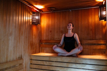 Happy relaxed woman in dark swimwear sitting on the bench in the hot sauna at the spa center and...