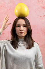 A woman trying to hold a whole pomelo fruit on her head. Balance concept.