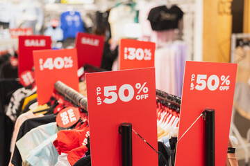 Red discount signs on clothes racks in a clothing store.