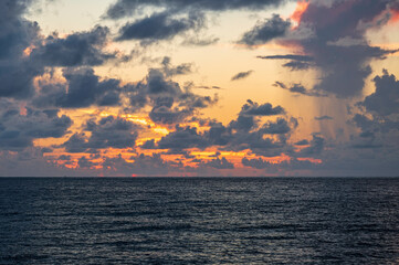 A view of the sunrise over the ocean off Miami Beach, south Florida. Tropical clouds fill the sky, and a small rainstorm can be seen on the horizon.